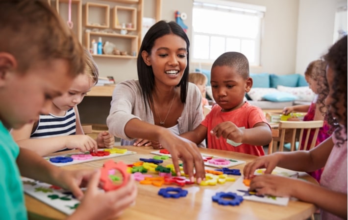 A teacher at a table of kids playing with colourful shapes at a Montessori school