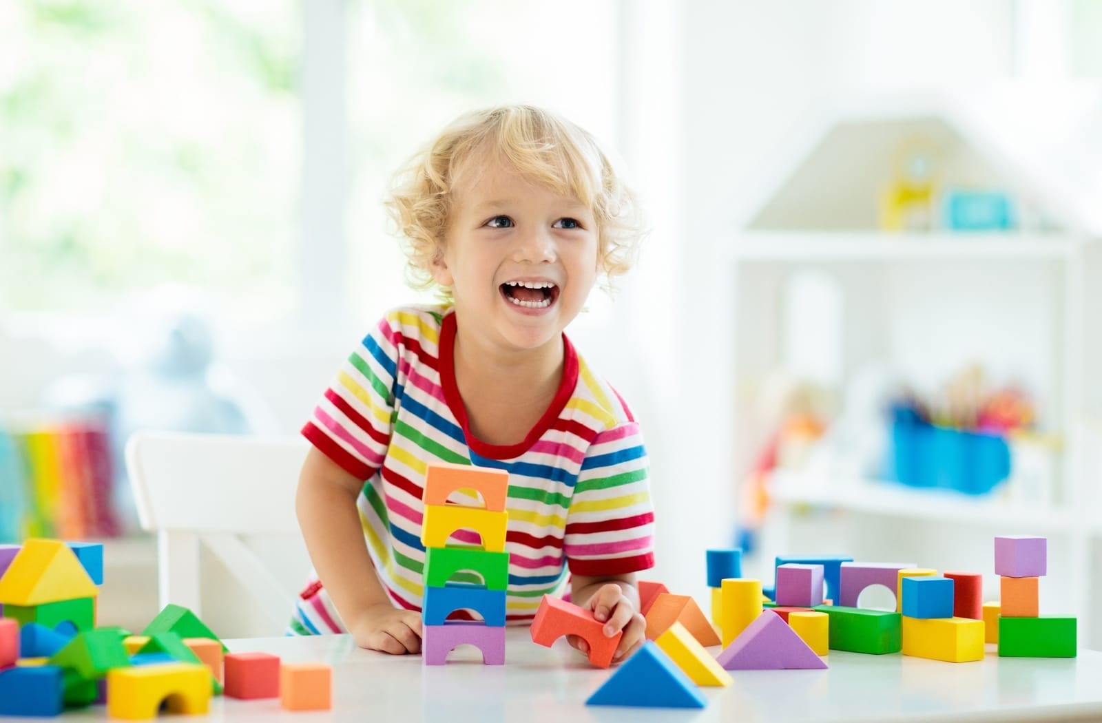 A young child with a colourful shirt smiling, having fun and playing with toys at a daycare